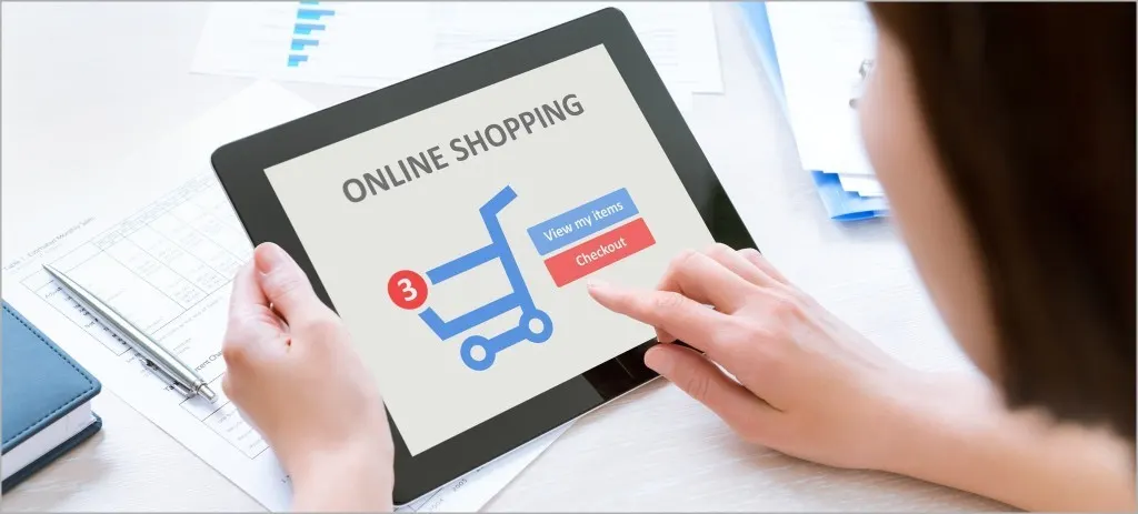 A woman shopping online on a tablet that shows a cart with three items and a checkout button