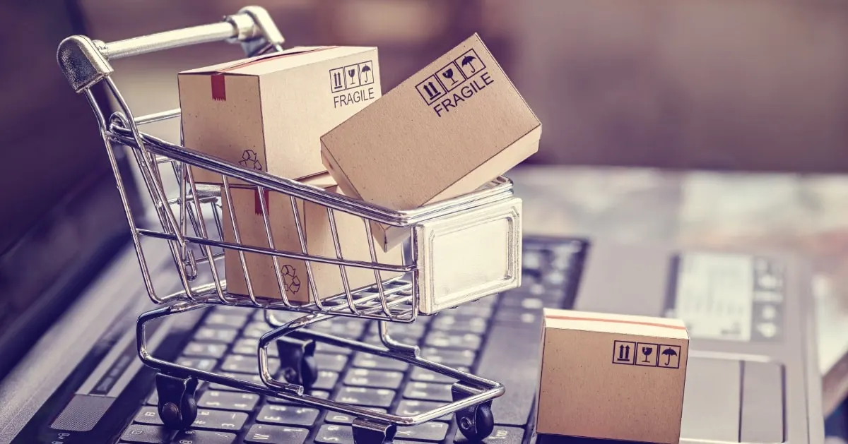 Miniature shopping cart holding cardboard parcels on a laptop keyboard