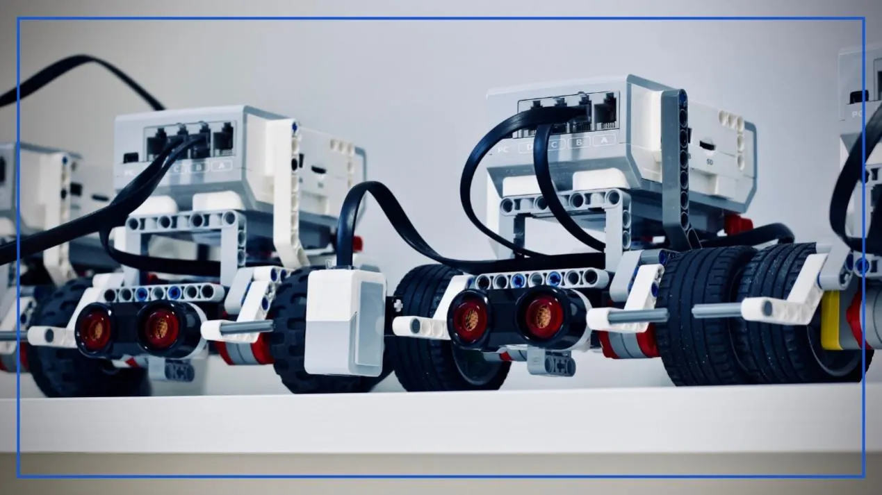 Row of educational robots built from white and gray construction blocks, with sensors and cables