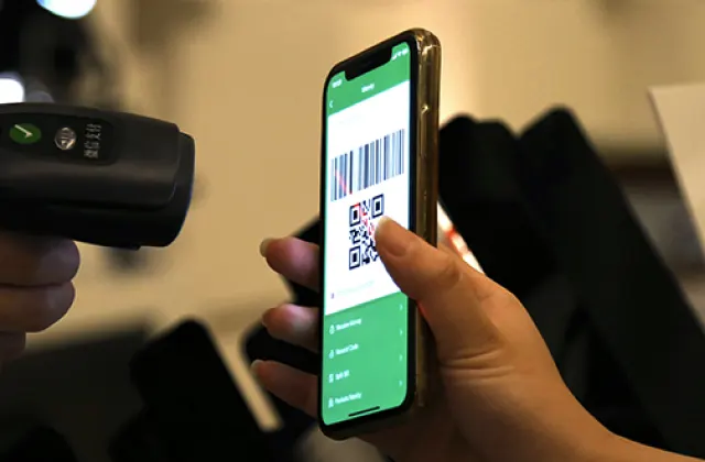A shopper holds up a WeChat Pay payment code on a phone to a merchant’s barcode scanner