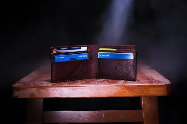 Open brown leather wallet holding bank cards, on a wooden stool