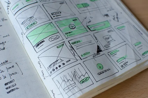 Notebook with hand-drawn wireframe sketches of web pages, highlighted in green