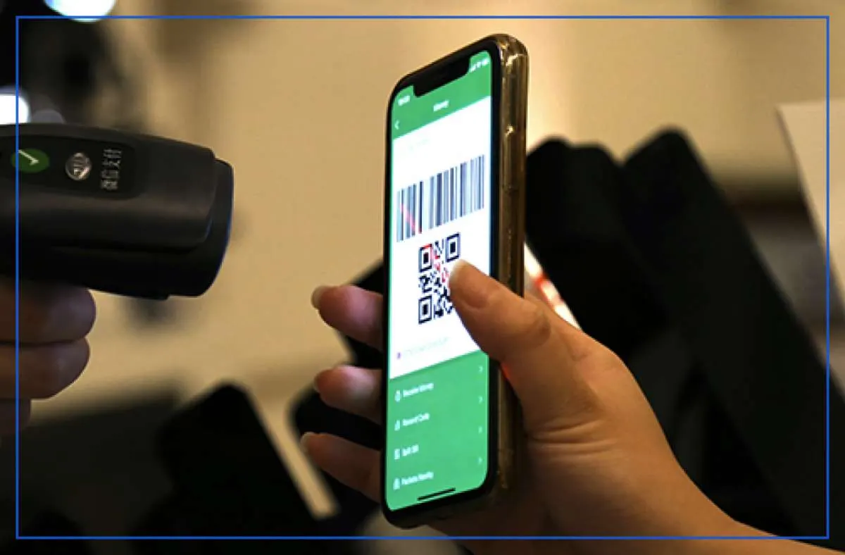 Shopper paying with a WeChat Pay QR code on a phone held up to a merchant’s barcode scanner