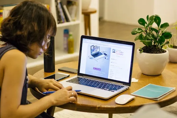 Woman taking notes next to a laptop displaying a website