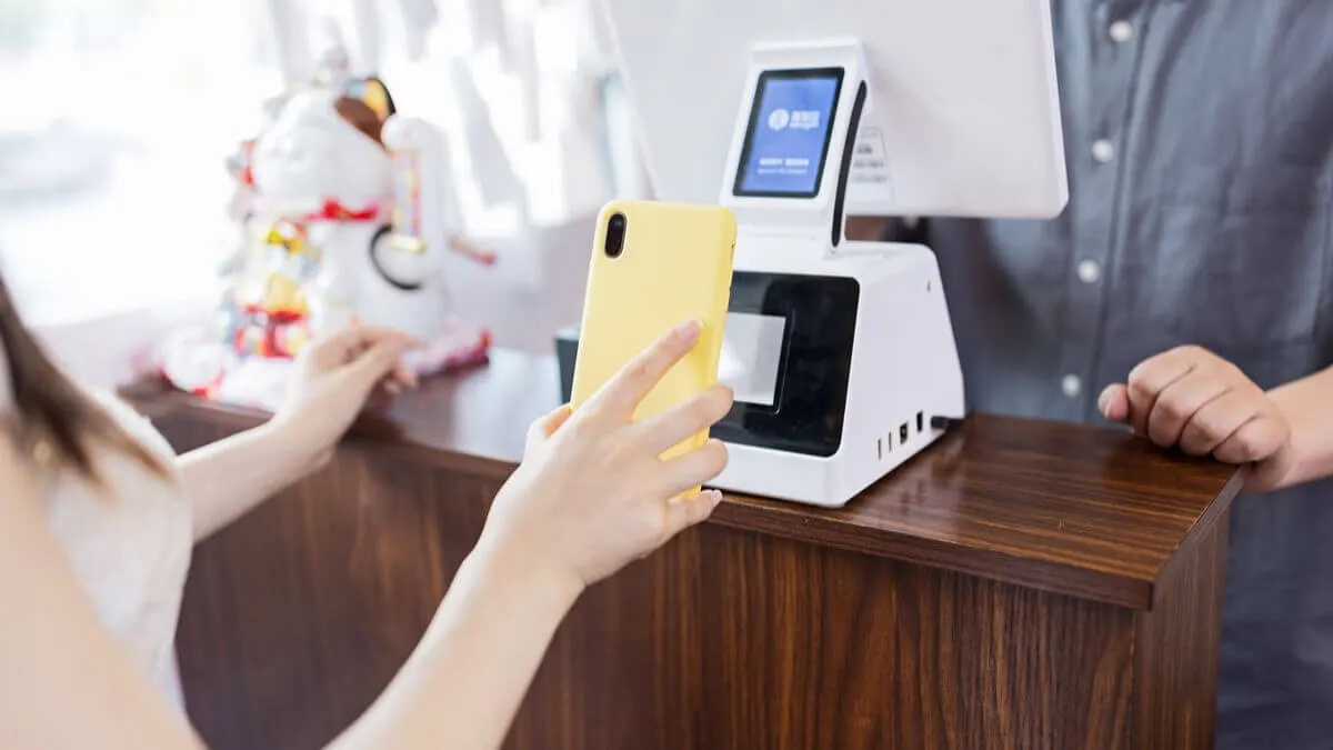 Customer holding a smartphone to a payment terminal at a shop counter