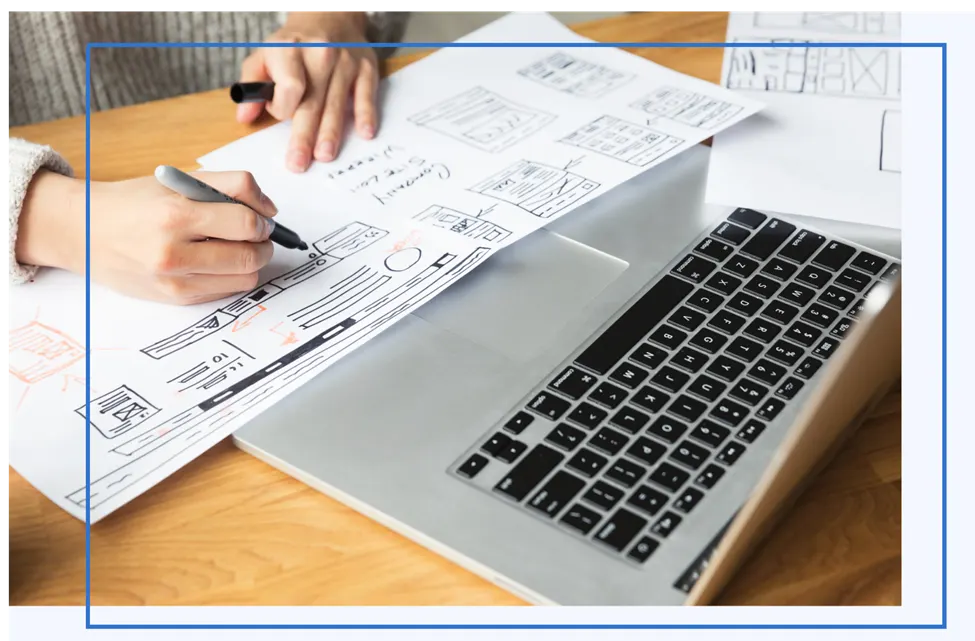 Hands sketching website wireframes on paper next to a laptop