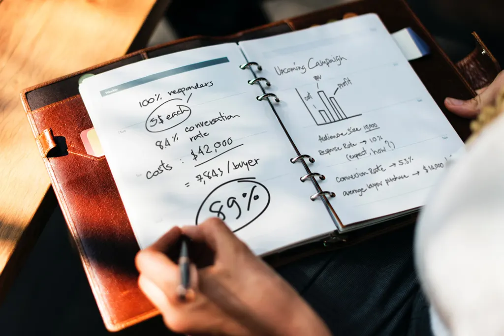 Hand writing campaign figures, costs and conversion rates in a notebook