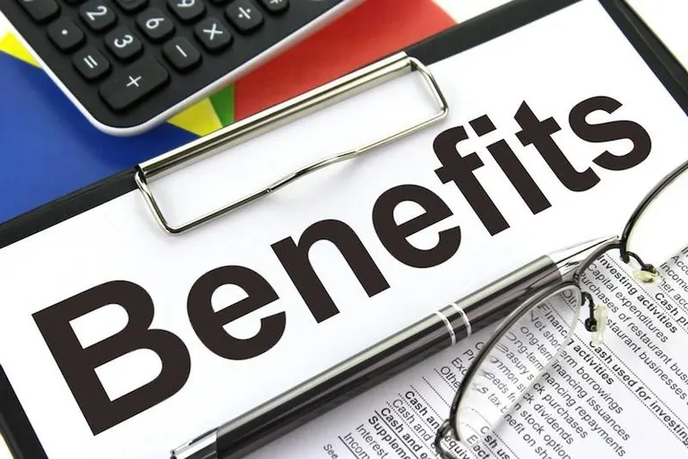 Clipboard with the word Benefits printed in large letters, next to a pen, glasses and a calculator