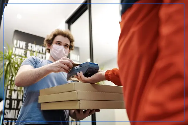 A masked rider handing a parcel to a customer